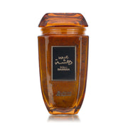 A glass jar with a brown liquid inside, presumably the Dahsha Bakhoor, with a black label on the front and a wooden lid on top.